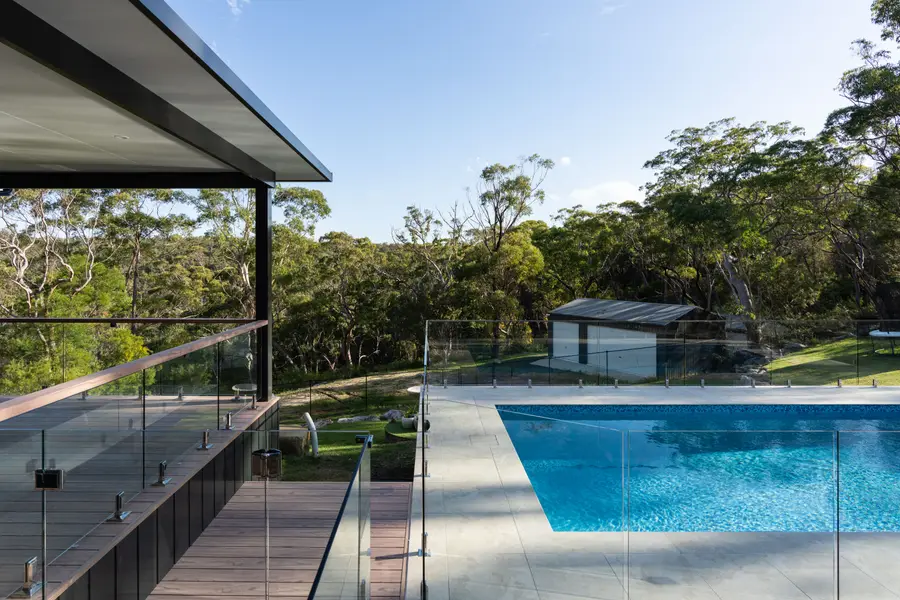 Deck and glass balustrade with a timber-look top rail, looking across the pool into the bush