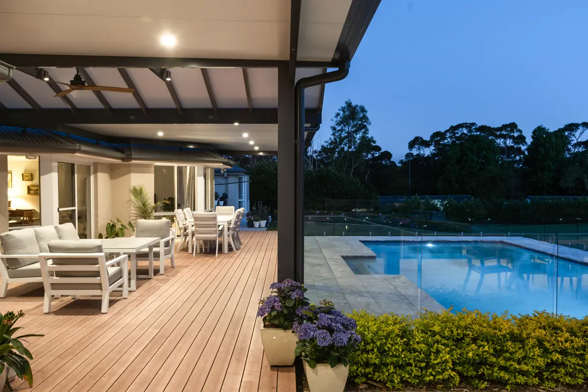 Deck running along the house under the pergola at dusk, pool and glass fencing alongside