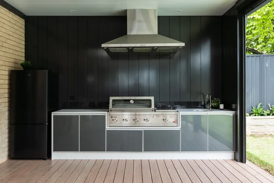 Outdoor kitchen with a stainless range hood run through the black clad wall above the barbecue