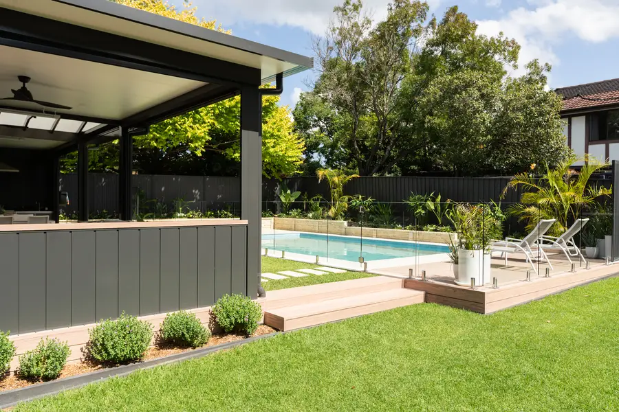 The clad wall running the length of the alfresco, with the deck stepping down to lawn and pool