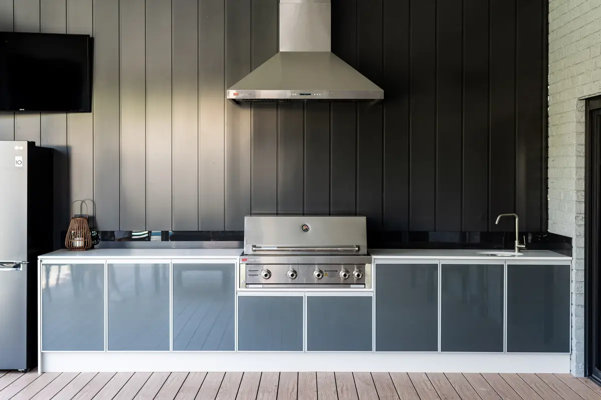 Clad wall serving an outdoor kitchen — range hood and wall-mounted TV both run through the aluminium frame