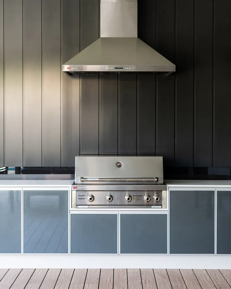 Charcoal vertical-panelled clad wall behind a built-in outdoor kitchen with barbecue, rangehood and wall-mounted TV
