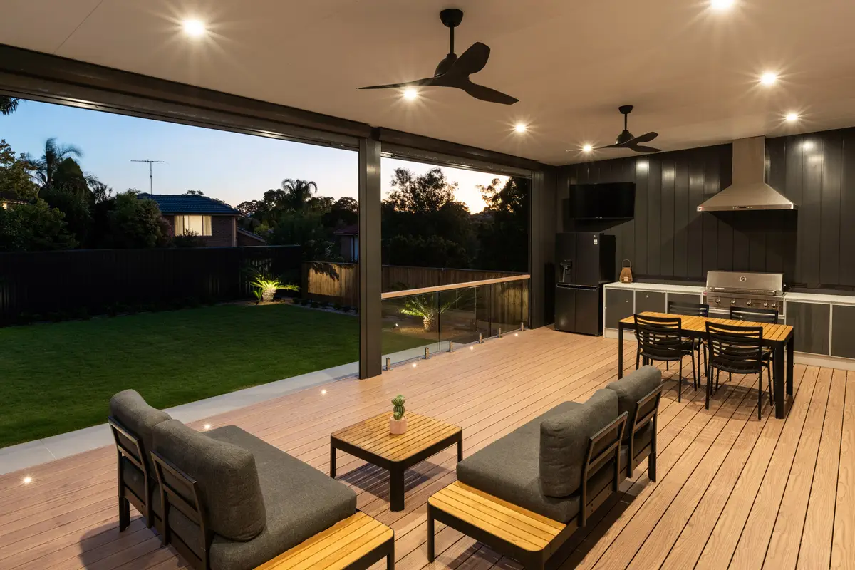 Alfresco lit at dusk with twin ceiling fans and an outdoor kitchen, opening to the deck and lawn, Dural