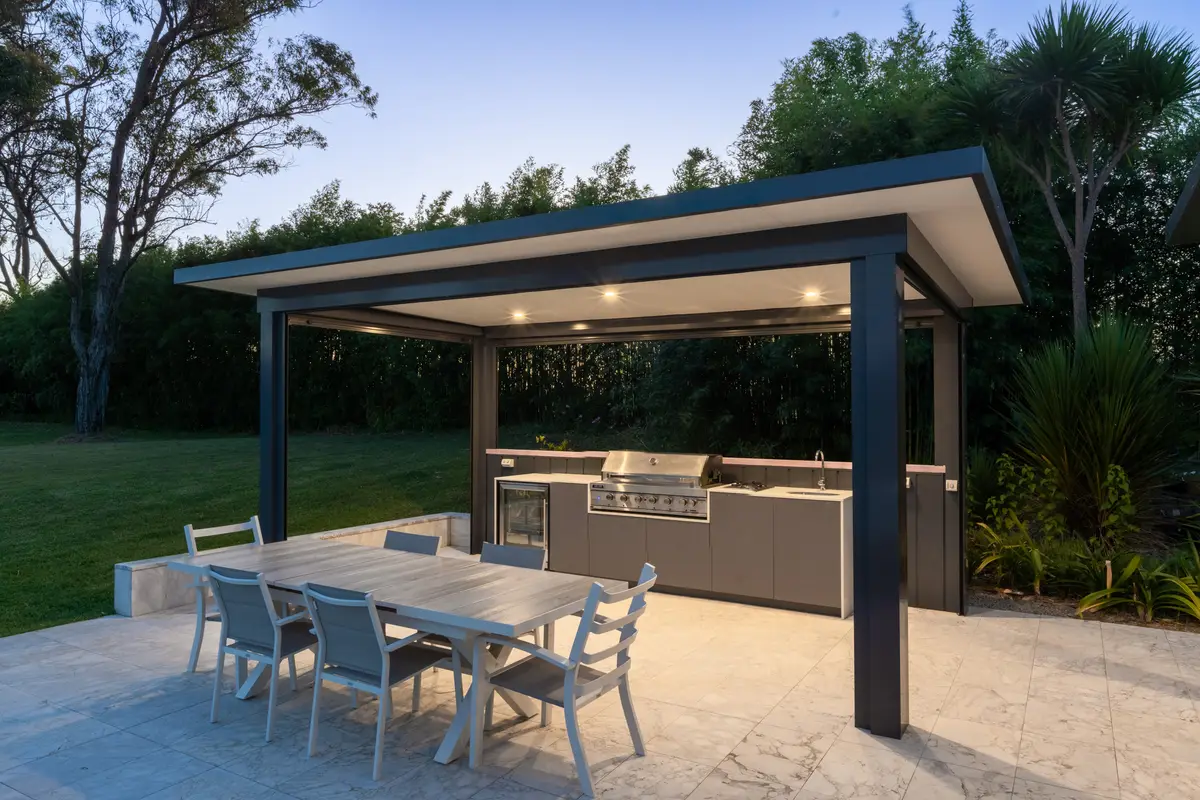 The cabana kitchen lit from within at dusk, against the bamboo hedge, Annangrove