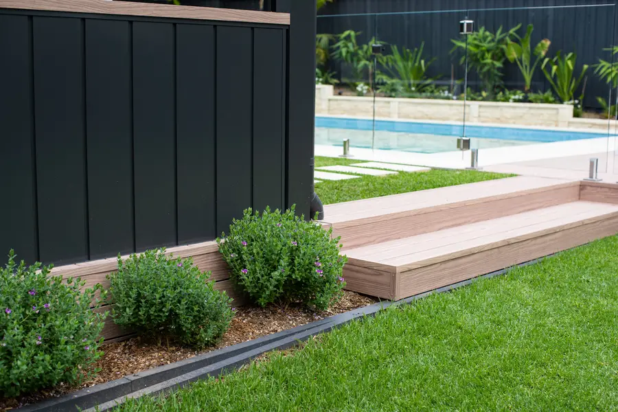 Dark powder-coated clad wall with a timber-look aluminium capping, beside the aluminium deck step and pool
