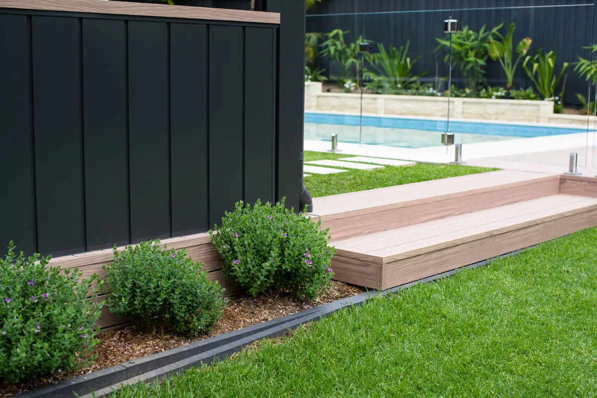 Aluminium clad wall in dark powder coat with a timber-look capping, running down to the deck and pool
