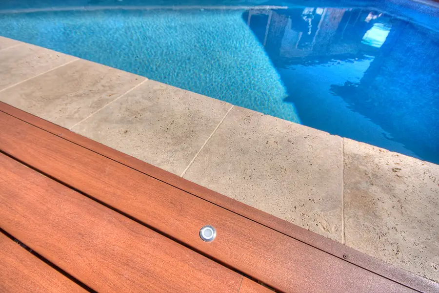 In-floor deck light set flush beside the travertine pool coping