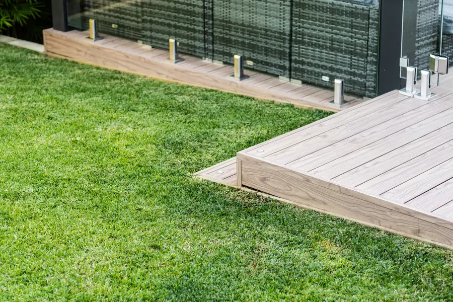 Close detail of the aluminium deck edge meeting the lawn, with in-floor lights along the border