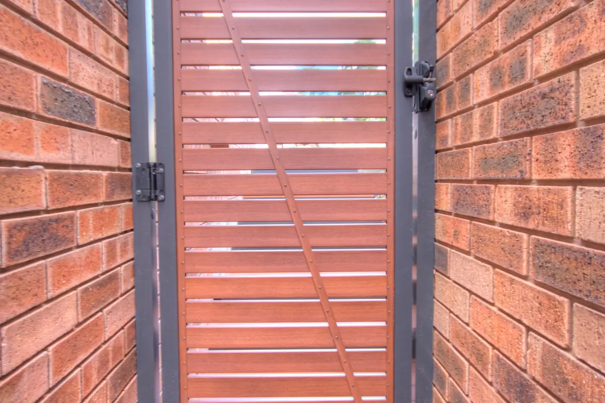Aluminium slat gate hung between two brick walls on a side access way, with a diagonal brace, three hinges and a latch