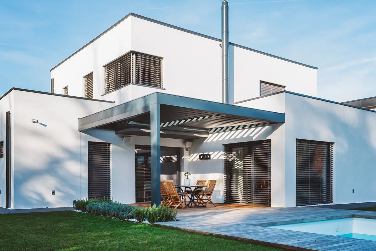 Louvred roof over an alfresco dining area set into the corner of a flat-roofed house beside a pool