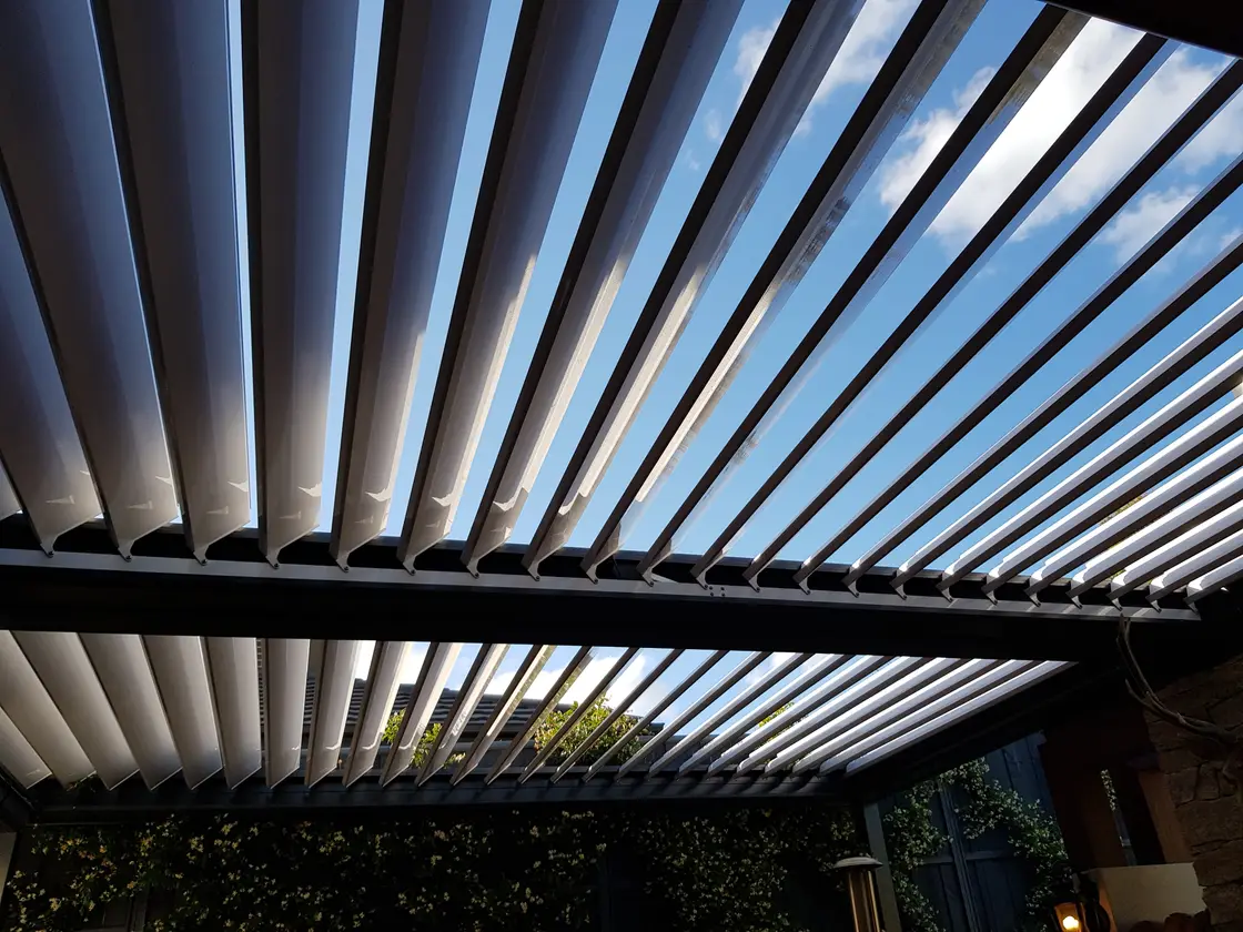 Looking up at a louvred roof with one section of blades open to the sky and the next closed, showing the range of rotation