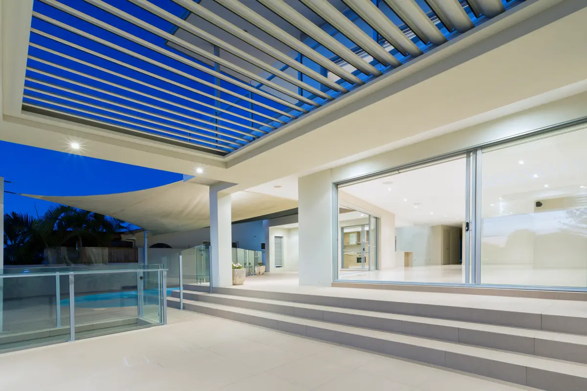 Louvred roof open to a twilight sky above a pool terrace, downlights lit in the beams