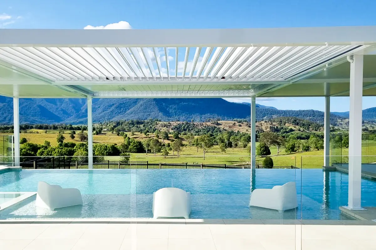 Louvred roof on slim posts over an infinity pool, looking out to open farmland and hills