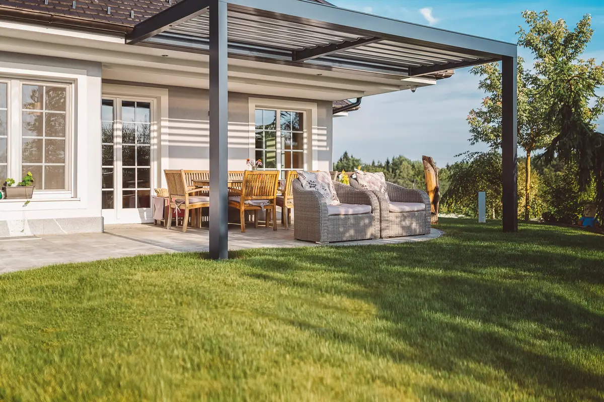 Dark-framed louvred roof over a paved patio with a timber dining setting, attached along the wall of the house