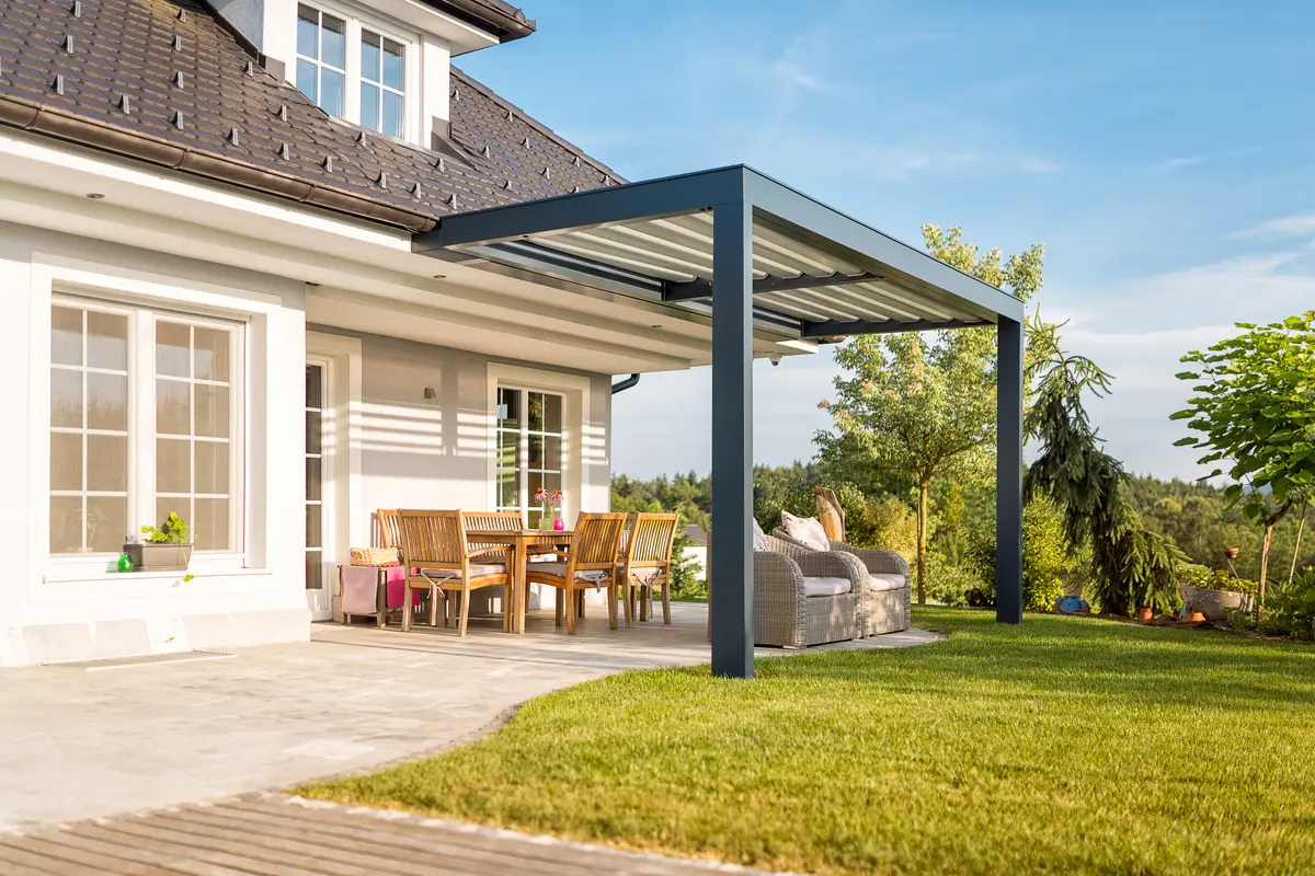 Louvred roof extending from the house over a patio and dining setting, seen across the lawn