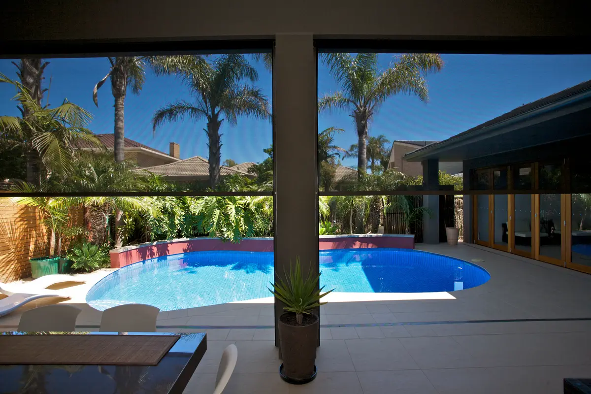 Looking out through a lowered mesh blind to a pool and palms, the view still completely readable through the weave