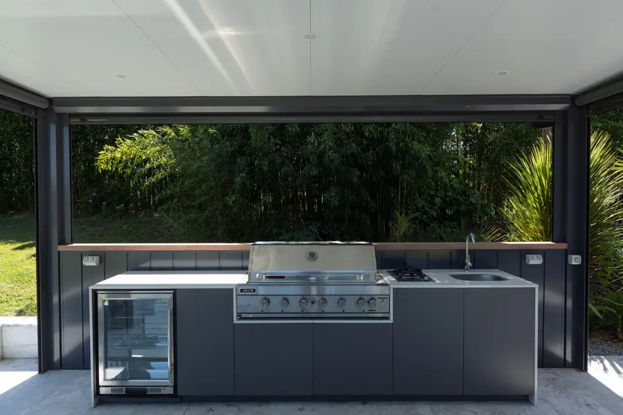 Barbecue, wok burner and sink built into the cabana's dark cabinetry with a timber top