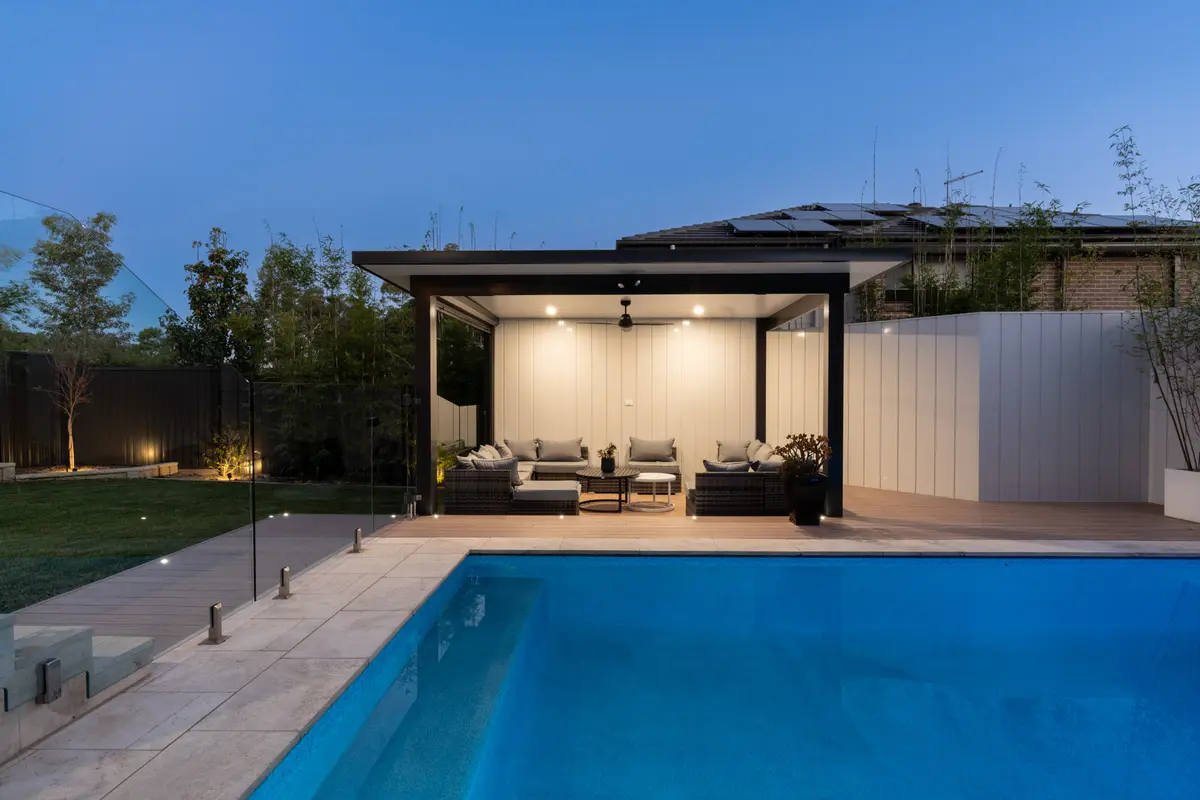 Freestanding pavilion lit from within at dusk, its clad wall glowing behind the lounge, North Kellyville