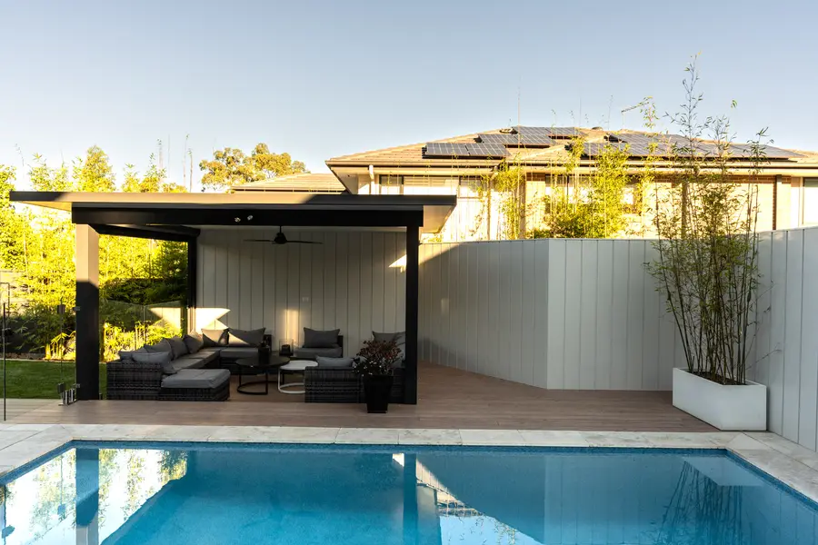 The freestanding pavilion across the pool, clad in pale powder-coated panels
