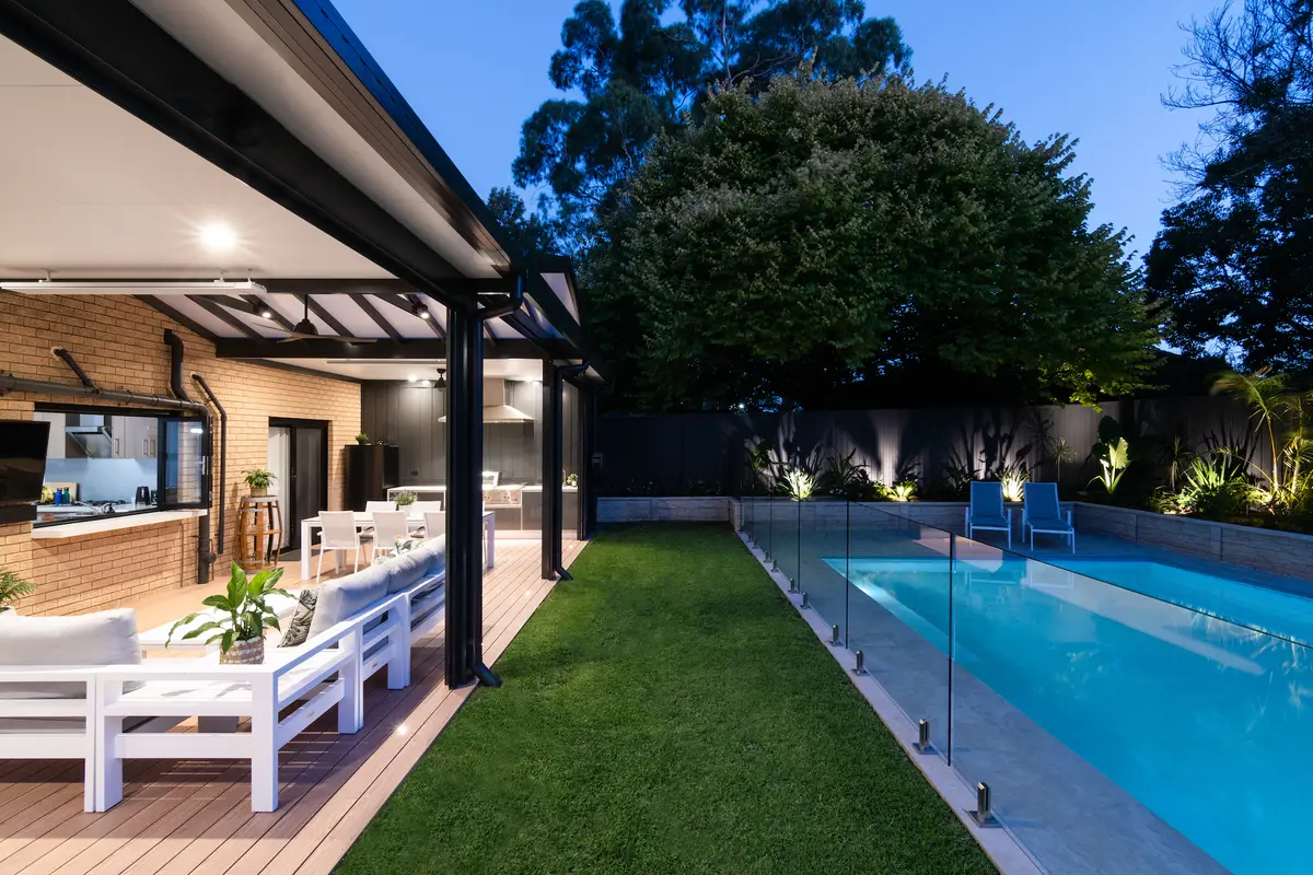 Outdoor kitchen under the pergola with a range hood run through the clad wall, lit at dusk, Cherrybrook