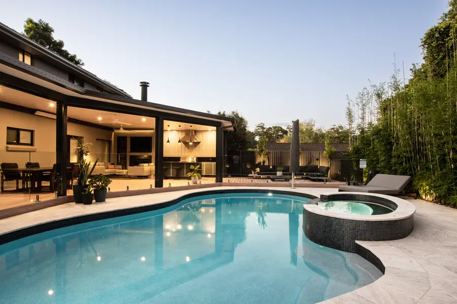 The figure-eight pool and raised spa at dusk, the alfresco glowing behind