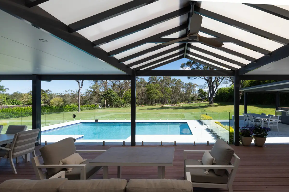 Under the gable pergola on exposed black beams, looking across the deck to the pool and paddocks, Annangrove
