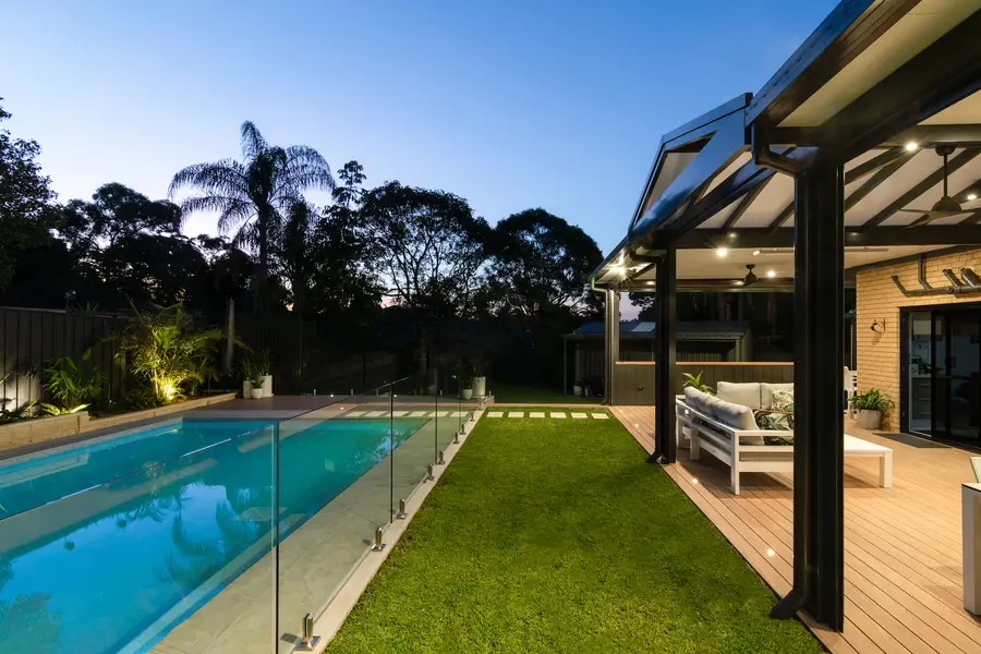 Gable pergola lit by downlights at dusk, looking across the lawn from the pool
