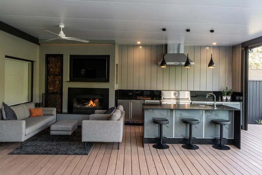 The outdoor room with the fire lit — wood-burning fireplace, TV and full outdoor kitchen under one roof