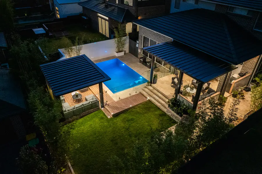 The backyard from above at dusk, the pool lit between the two roofs