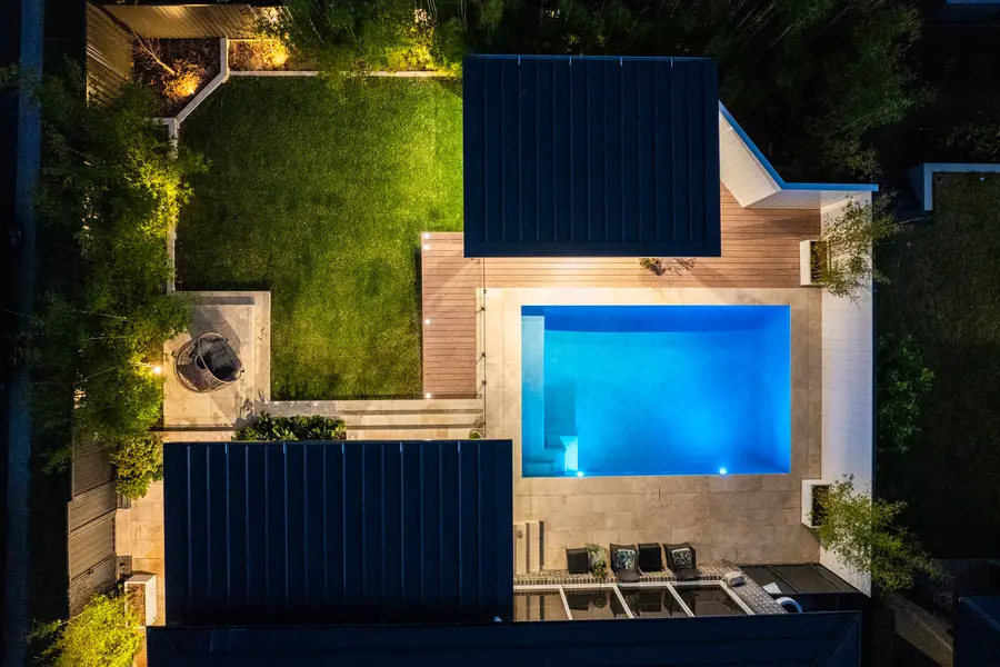 Directly overhead at dusk — the two roofs, the lit pool and the lawn between
